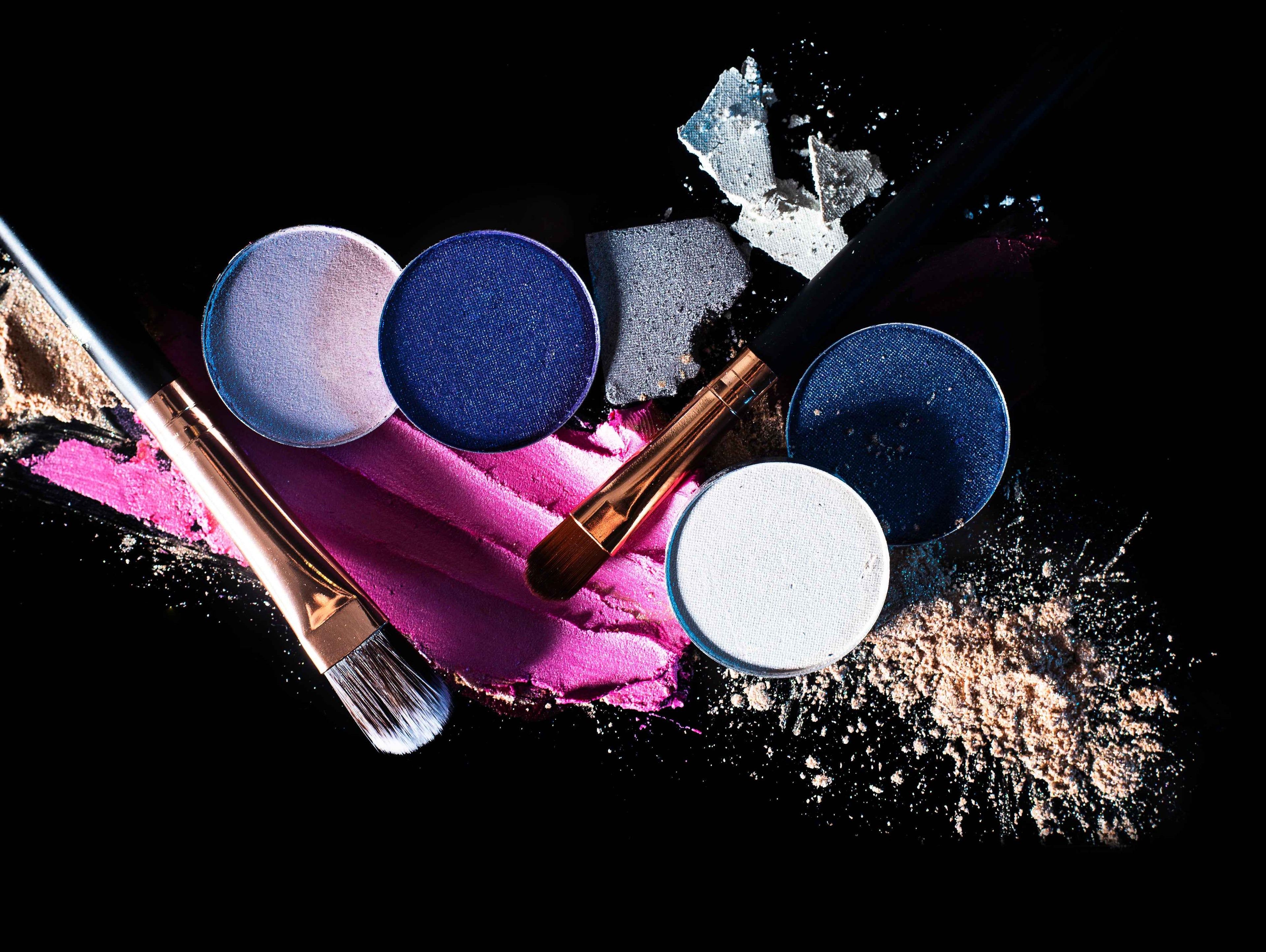 Assorted makeup products and brushes with colorful powder on black background